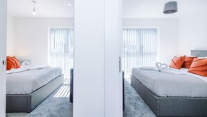 Un dormitorio moderno con cama, almohadas, una mesita de noche y una ventana con persianas.