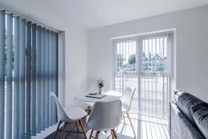 A modern room with a dining table, chairs, a sofa, and a large window with blinds. - Stylish 2BDR Hospitals Nearby Free Parking (Liverpool)