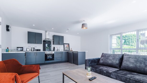 Una cocina moderna con armarios oscuros, una isla central y una zona de comedor con sofá y una mesa de centro.