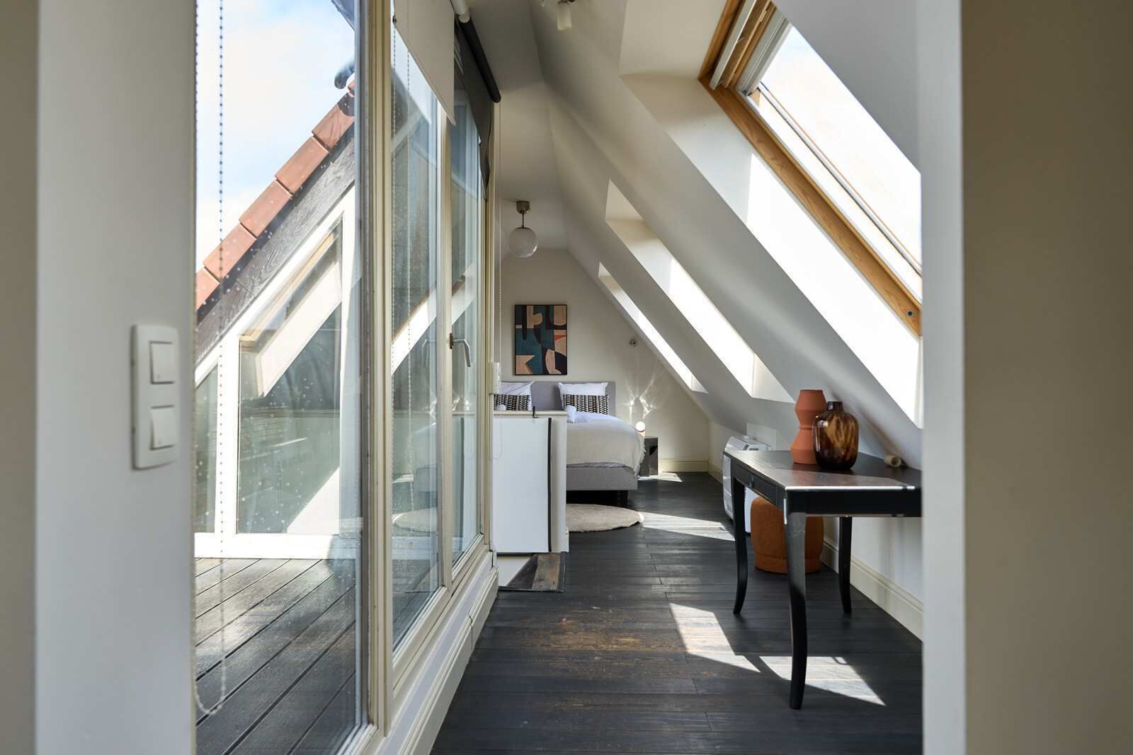 Een kamer met hoge plafonds, dakramen, een bed, een bureau en een stoel.
