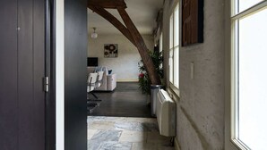 En gang med synlige træbjælker i loftet, et siddeområde med sofa og stole, samt en potteplante.