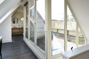 Ein Zimmer mit Oberlicht, Holzboden, Badezimmer mit Waschbecken und Spiegel sowie Blick auf eine Holzterrasse.
