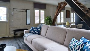 En stue med sofa, bænk, sofabord og trappe.