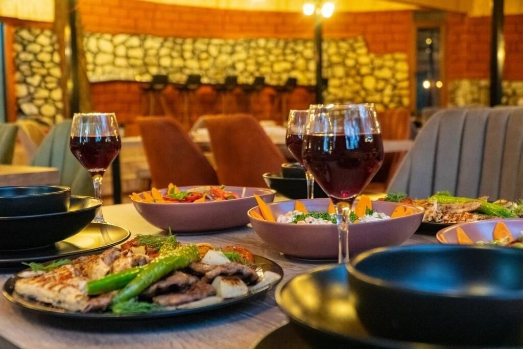 A restaurant setting with multiple tables, each with plates of food and glasses of red wine.