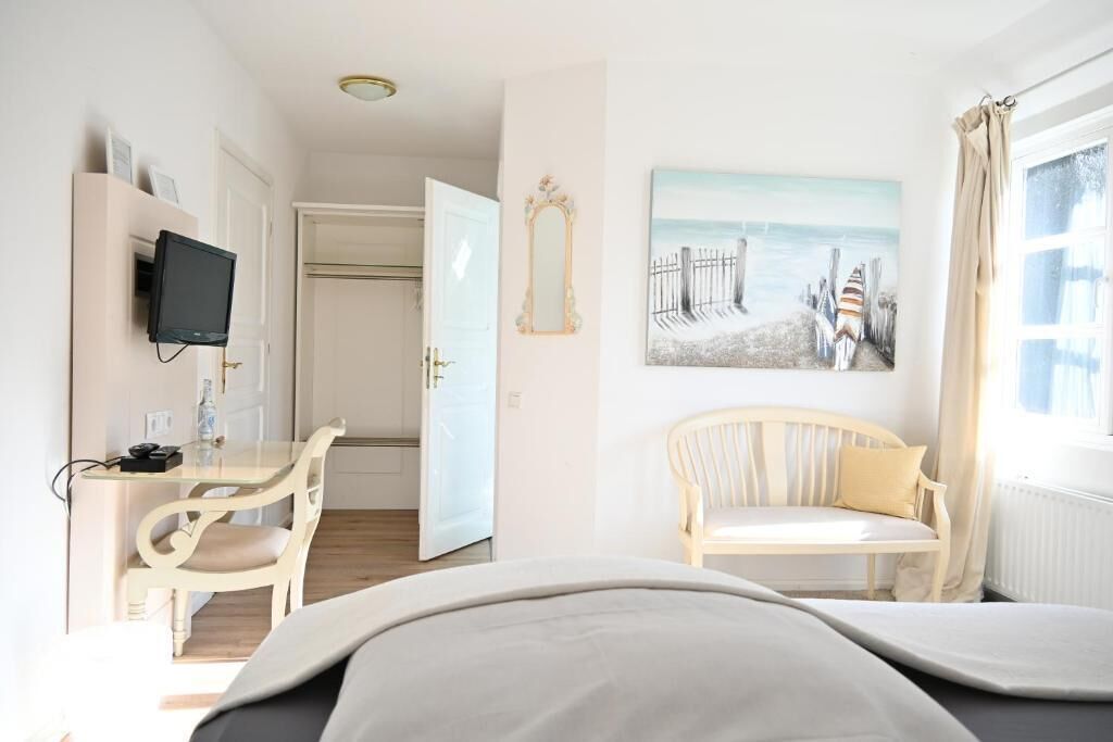 Ein Hotelzimmer mit Bett, Schreibtisch mit Stuhl, Fernseher, einem Gemälde und einem Fenster mit Vorhängen.
