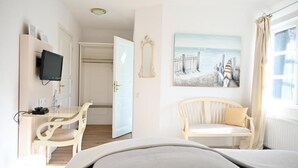 Et hotelværelse med en seng, et skrivebord med stol, et fjernsyn, et billede og et vindue med gardiner.