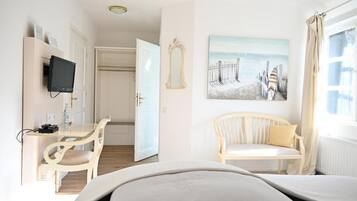 Ein Hotelzimmer mit Bett, Schreibtisch mit Stuhl, Fernseher, einem Gemälde und einem Fenster mit Vorhängen.