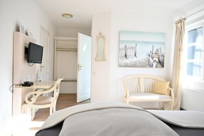 A hotel room with a bed, a desk with a chair, a television, a painting, and a window with curtains. - Landsitzhotel Peterhof  (Hodorf)