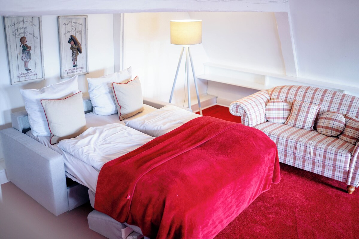 Un dormitorio con una cama, una colcha roja, un sofá blanco y una lámpara de pie.