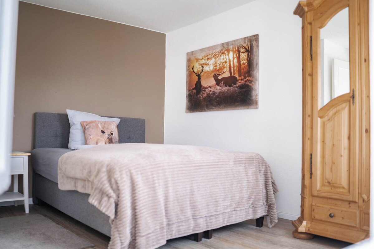 Un dormitorio con cama, mesita de noche, armario de madera y un cuadro de un ciervo en la pared.