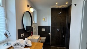 Et moderne badeværelse med et træbord, et rundt spejl, et toilet og en mørk bruseafdeling.