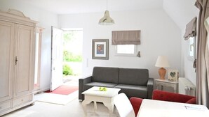 Et værelse med en grå sofa, et hvidt bord, en rød stol, et hvidt skab og en lampe på et natbord.