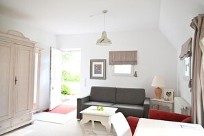 A room with a grey sofa, a white table, a red chair, a white cabinet, and a lamp on a side table. - Landsitzhotel Peterhof  (Hodorf)