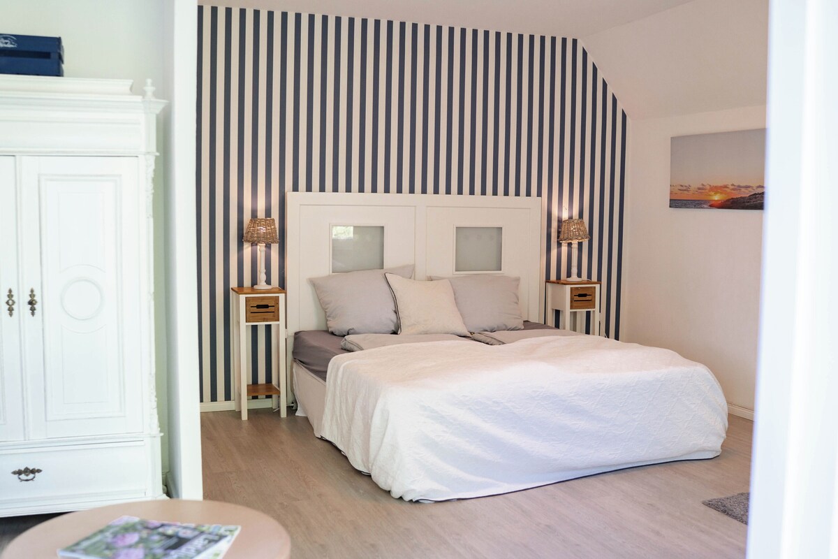Un dormitorio con cama, mesitas de noche, armario y pared a rayas.