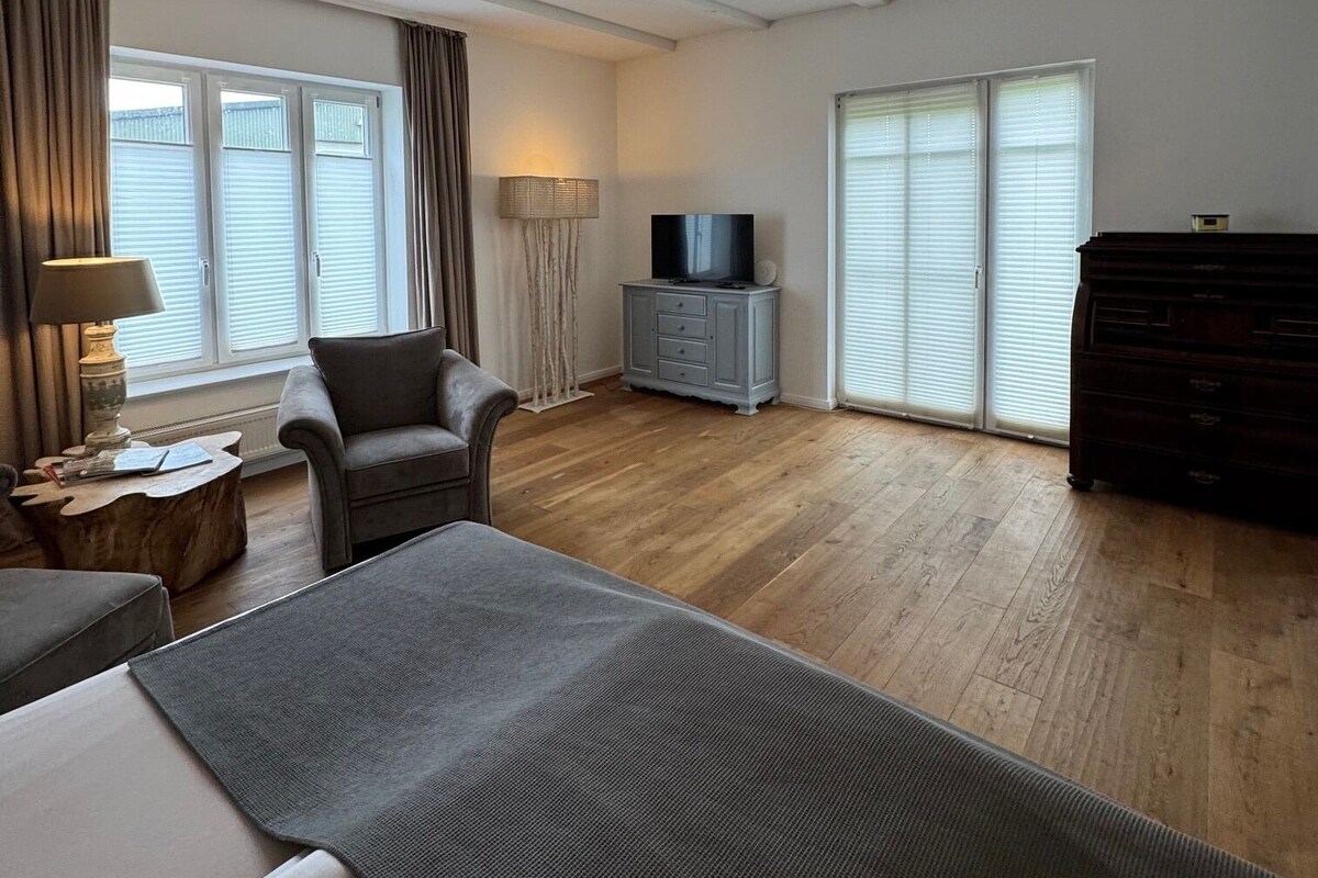 Una habitación amplia con una cama grande, un sofá, un televisor y un aparador.