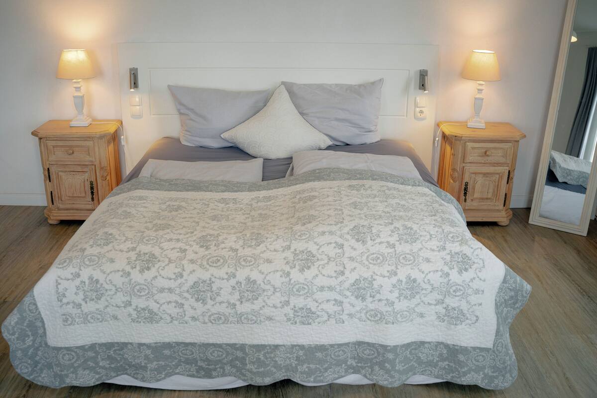 Ein Bett mit gemustertem Überwurf, zwei Nachttische mit Lampen und ein hölzernes Kopfteil.