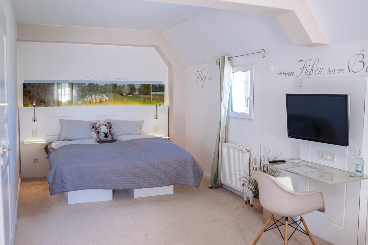 Un dormitorio con una cama, un escritorio, un televisor y una ventana con vista a un campo.