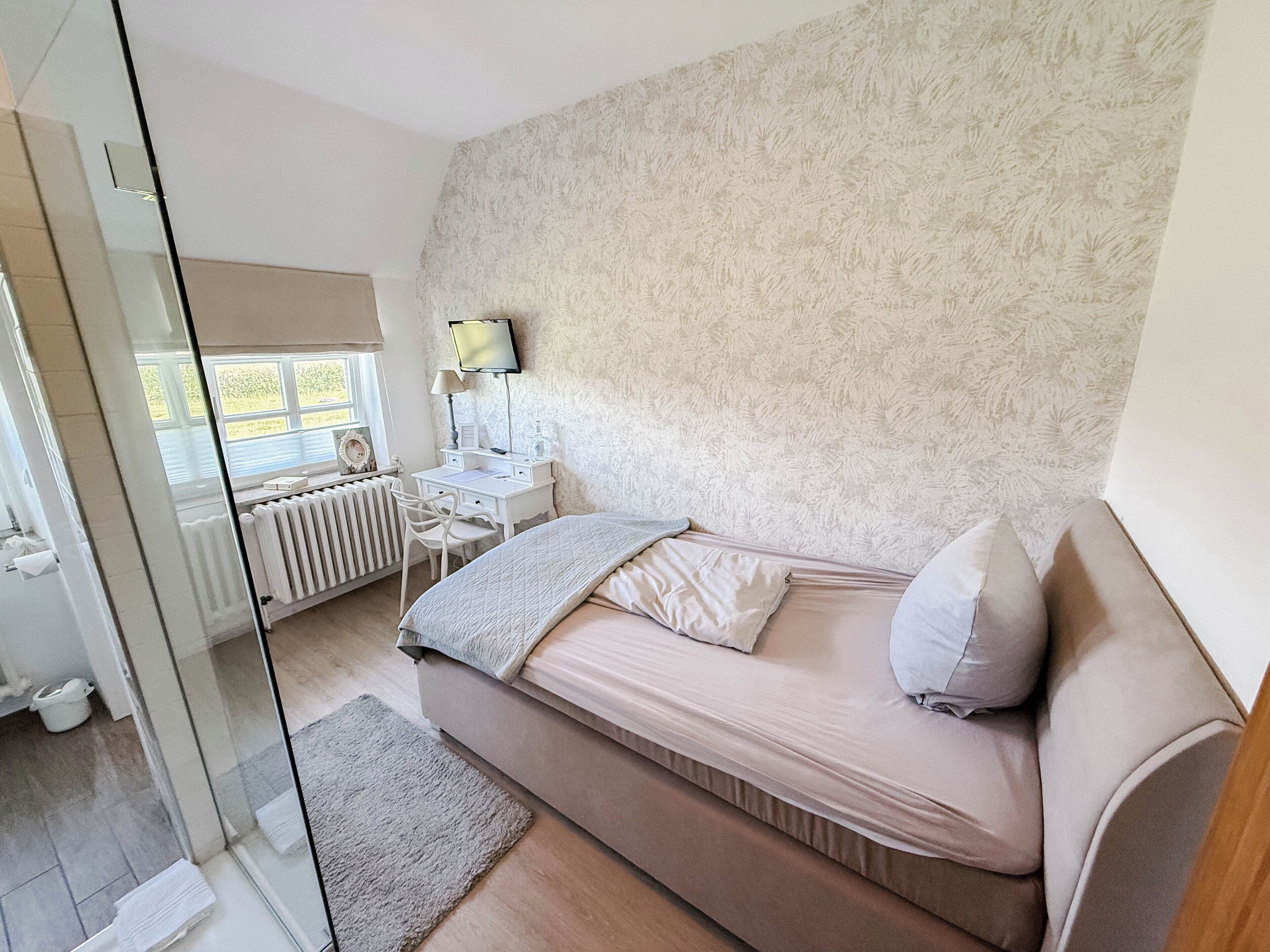 A bedroom with a bed, a desk, a chair, a radiator, and a window.