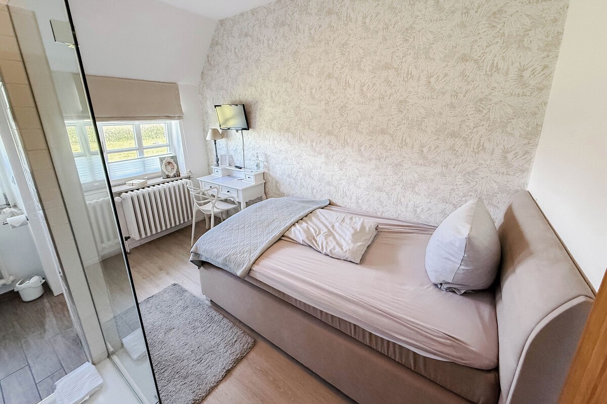 Un dormitorio con cama, escritorio, silla, radiador y ventana.
