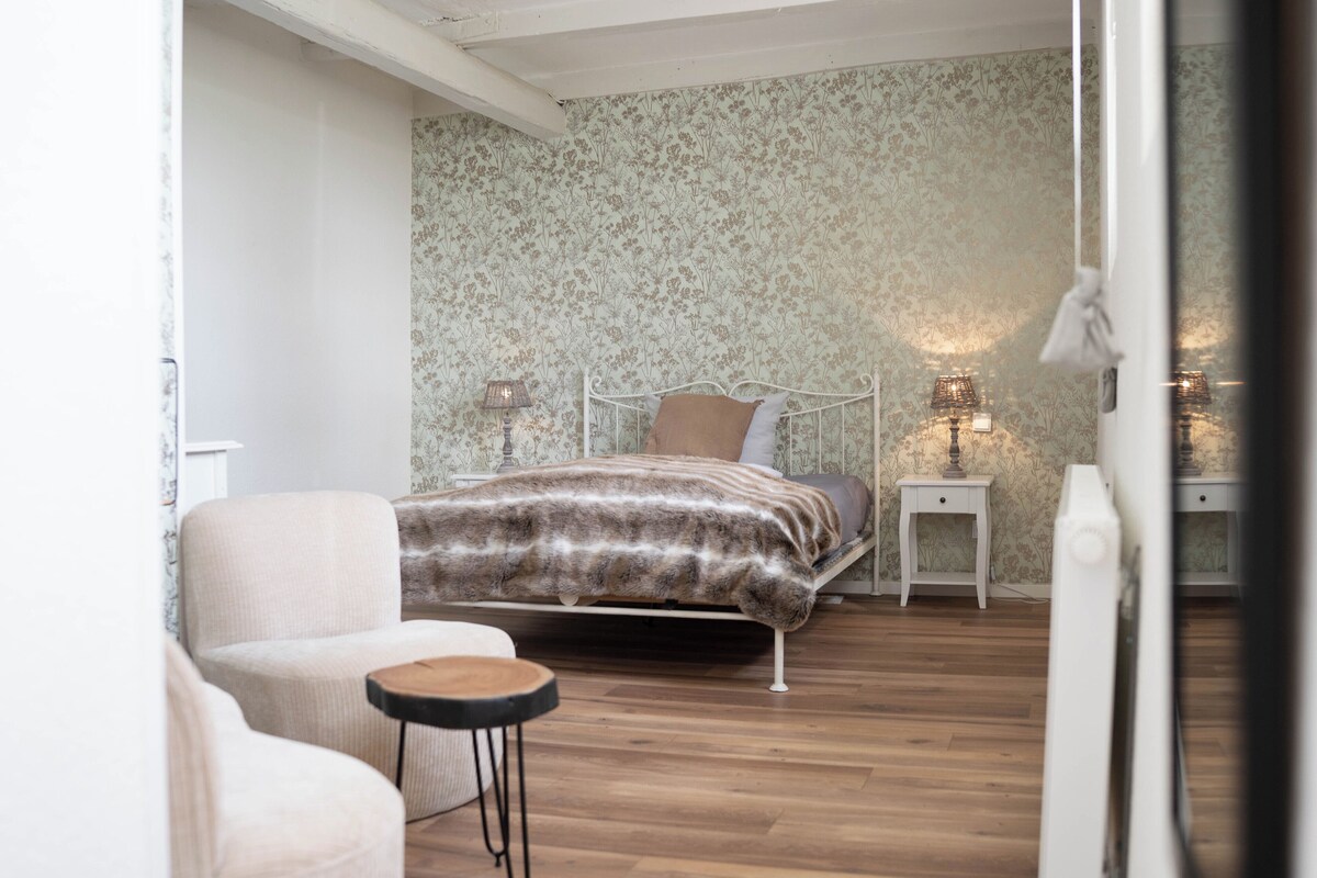 Un dormitorio con una cama, una silla, una mesita y dos lámparas de noche.