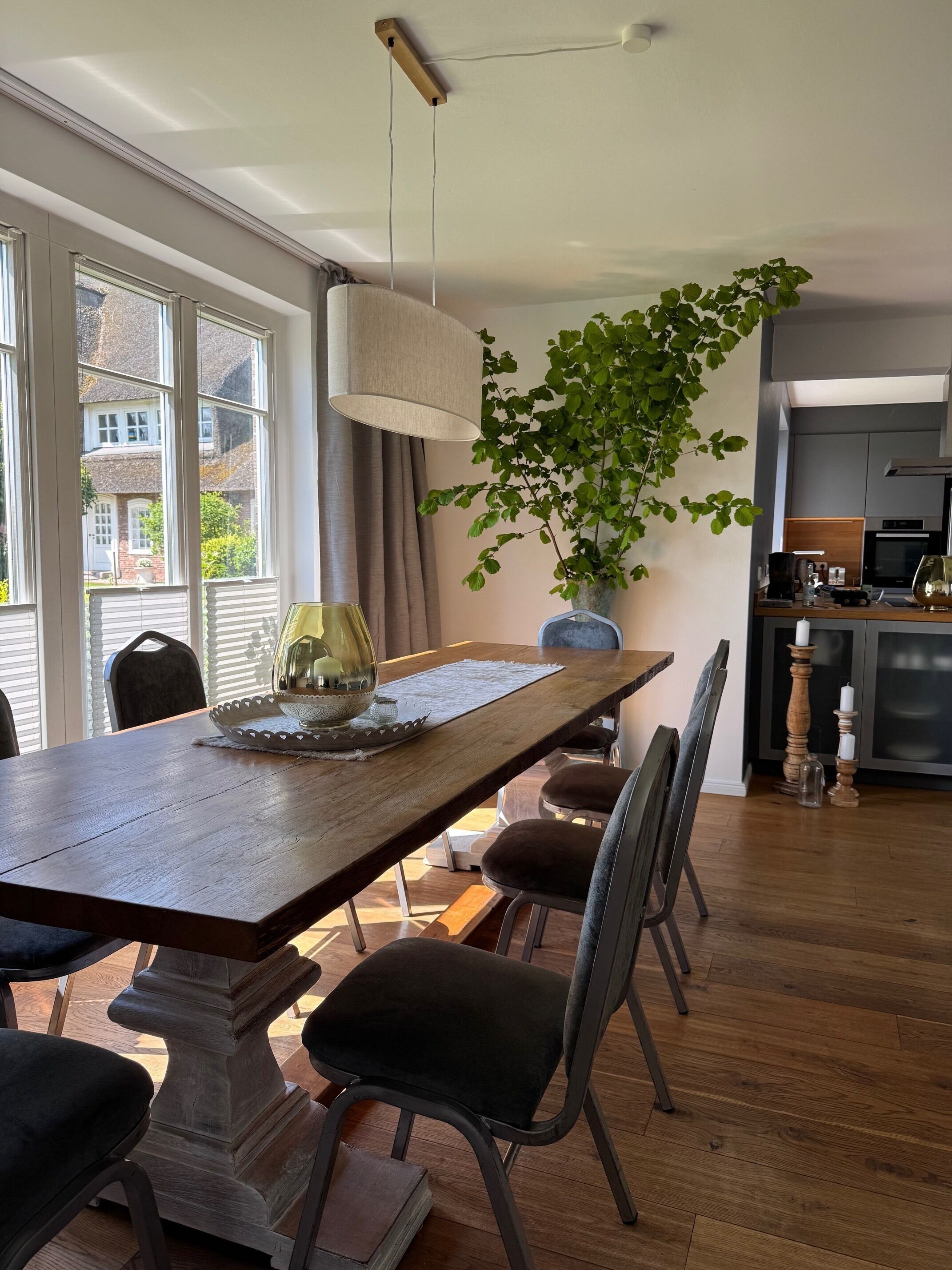 Ein Essbereich mit Holztisch, Stühlen, einer Pflanze und einer Küche im Hintergrund.