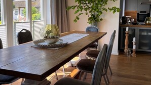 Et spiseområde med et træbord, stole, en plante og et køkken i baggrunden.