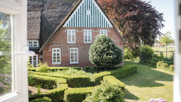 Et traditionelt hus med et stejlt tag, en murstensfacade og vinduer med hvide rammer.