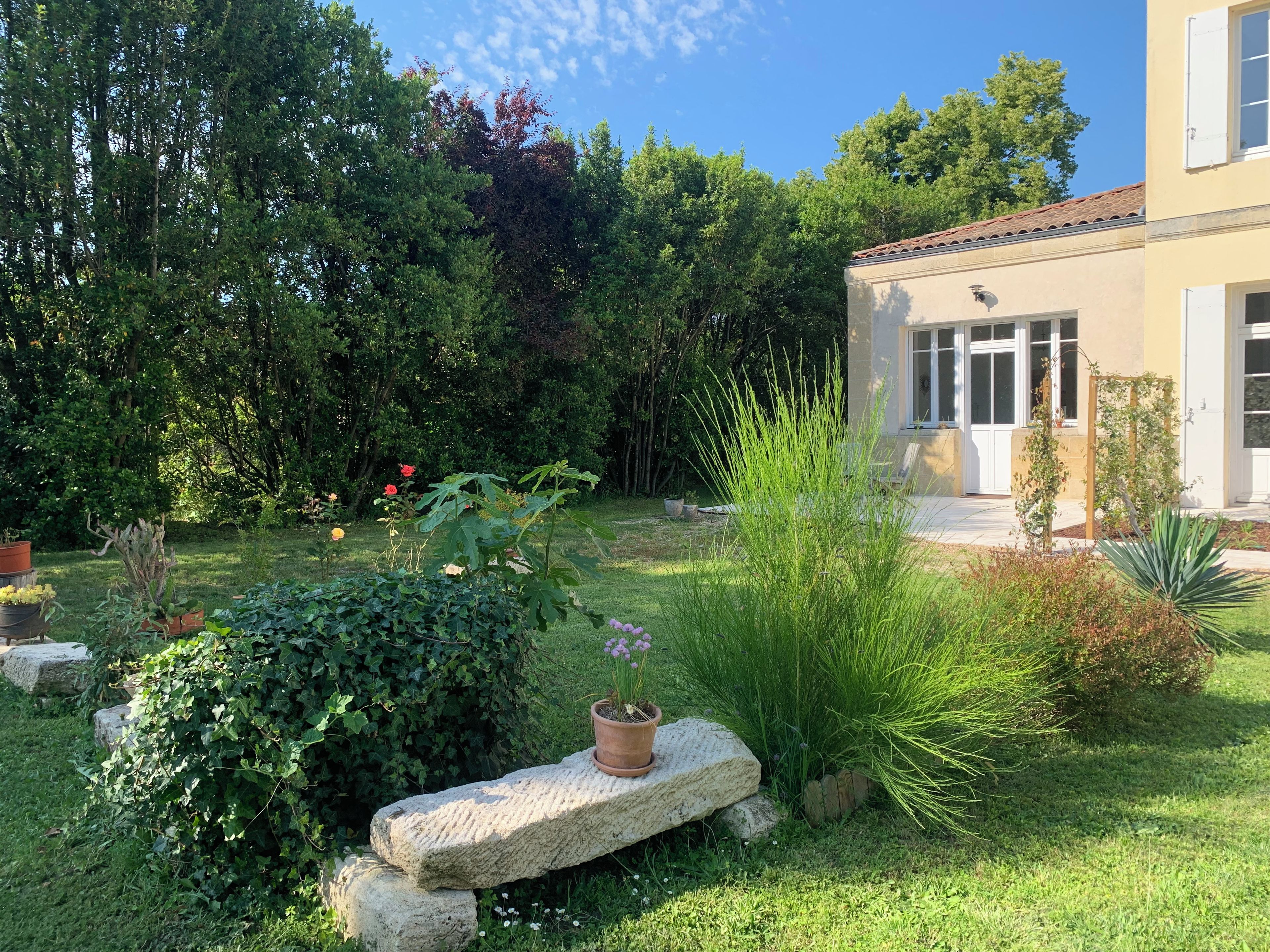 A garden with a stone bench, potted plants, and a building with a tiled roof.
