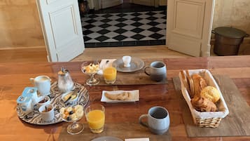 Une table de petit-déjeuner avec divers aliments et boissons, un sol à carreaux et une vue sur une pièce où se trouvent un lit et une plante.