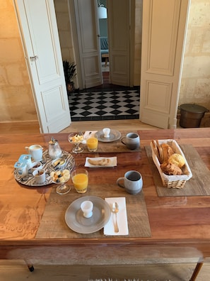 A breakfast table with various food items and drinks, a checkered floor, and a view into a room with a bed and a plant.