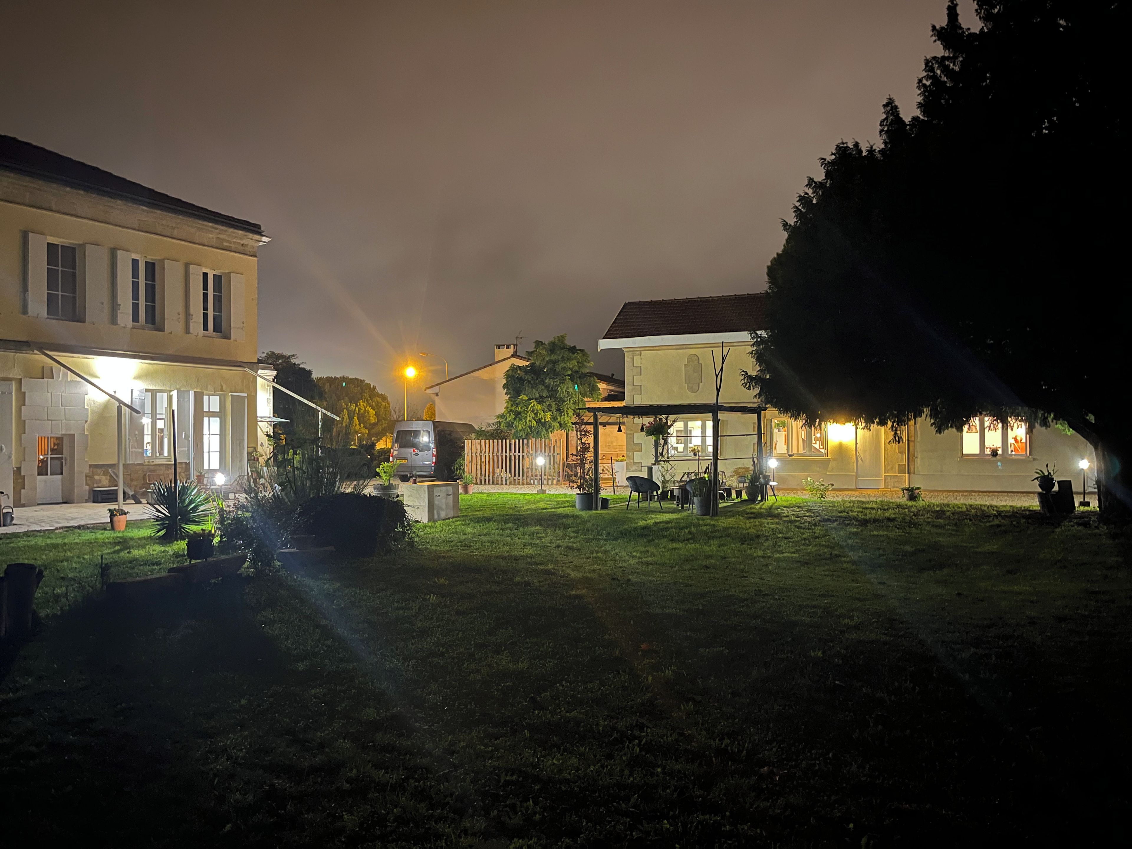 Een nachtbeeld van een woonwijk met een verlicht huis, een geparkeerde auto en een gazon.