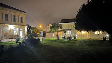 Een nachtbeeld van een woonwijk met een verlicht huis, een geparkeerde auto en een gazon.