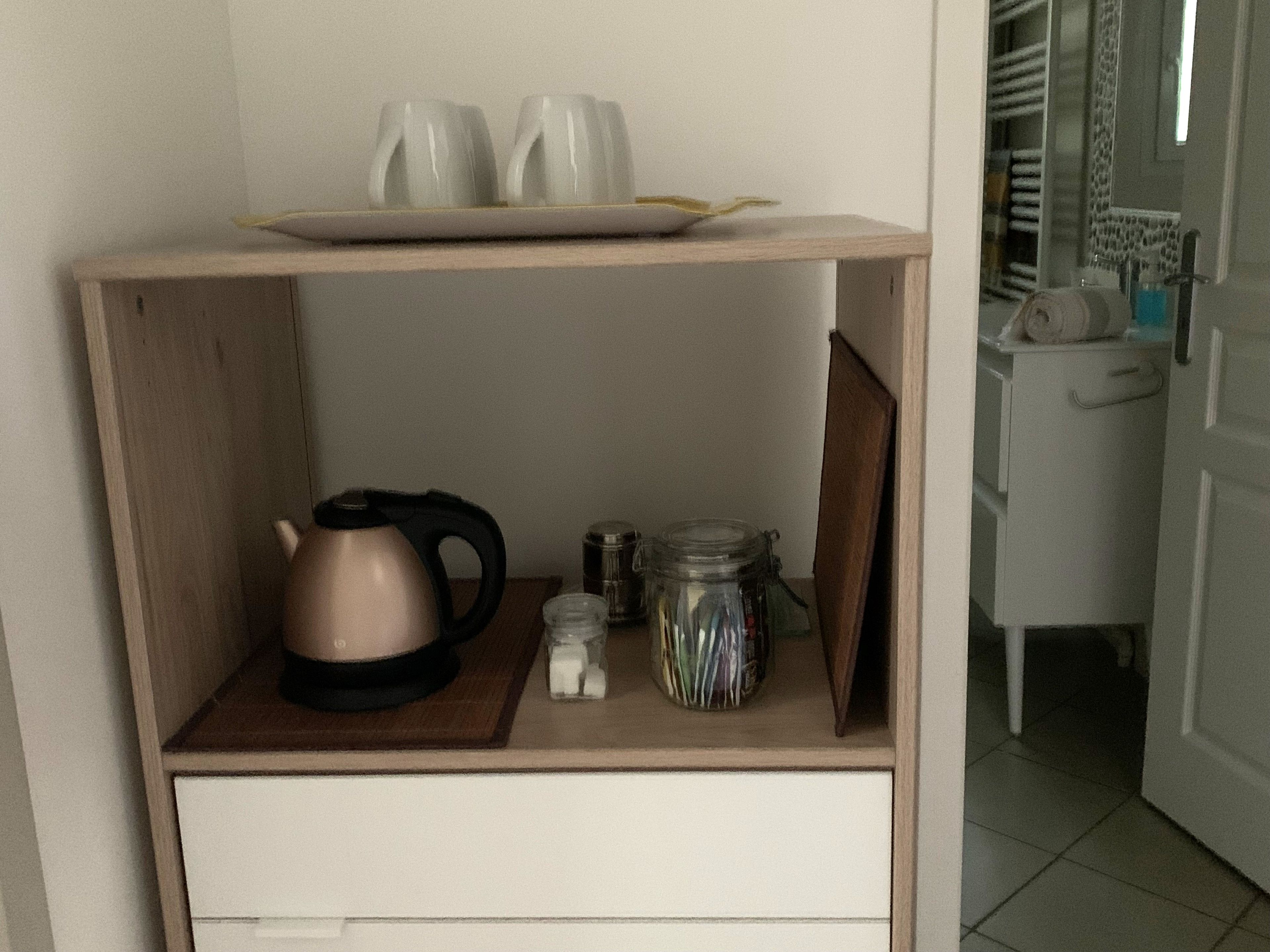 Ein kleines Holzregal mit einem Wasserkocher, einer Glaseinmachglas und einem Teller mit Tassen.
