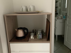 Une petite étagère en bois sur laquelle se trouvent une bouilloire, un bocal et une assiette avec des tasses.