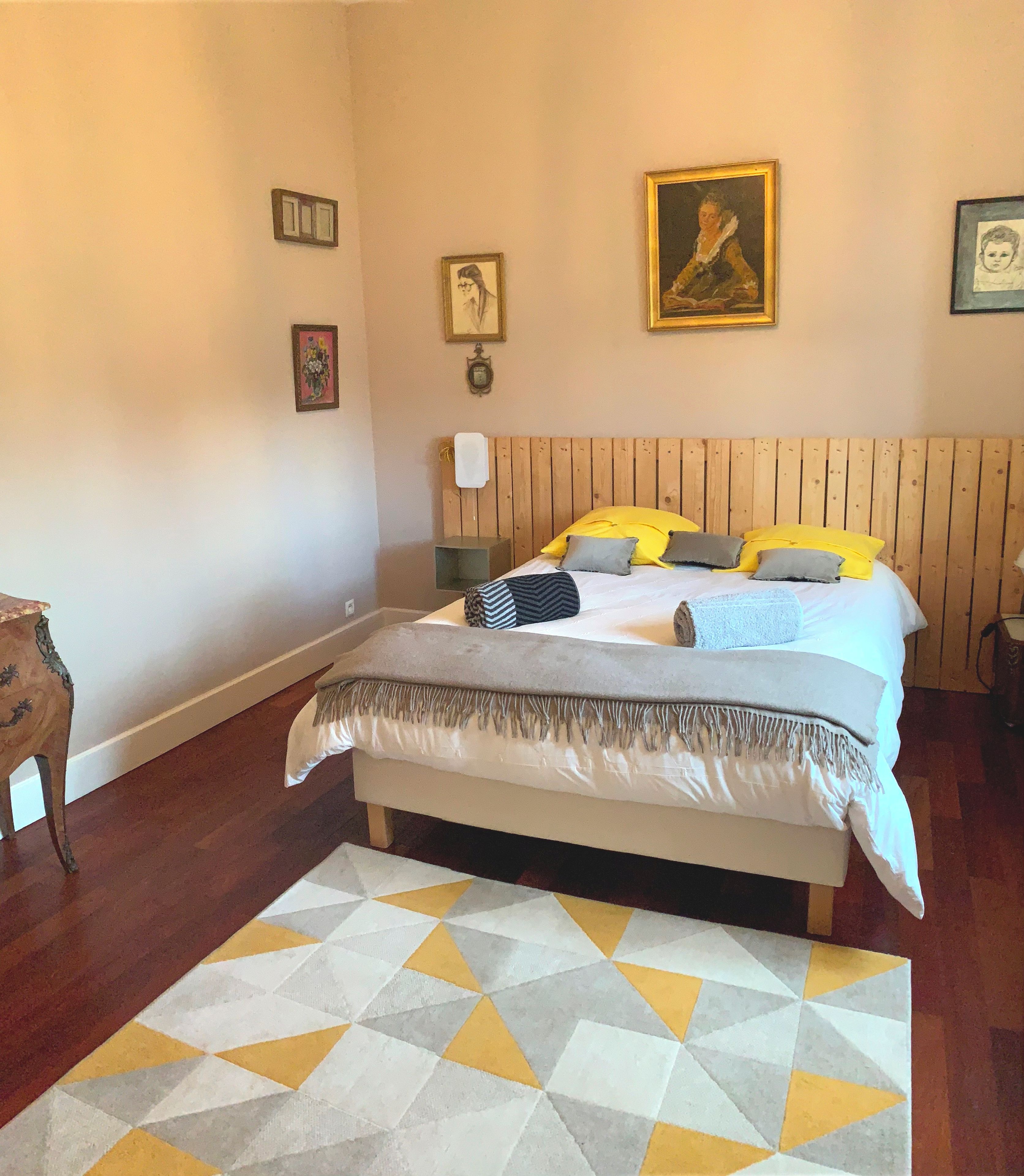 A bedroom with a bed, a wooden headboard, a patterned rug, and wall-mounted artwork.