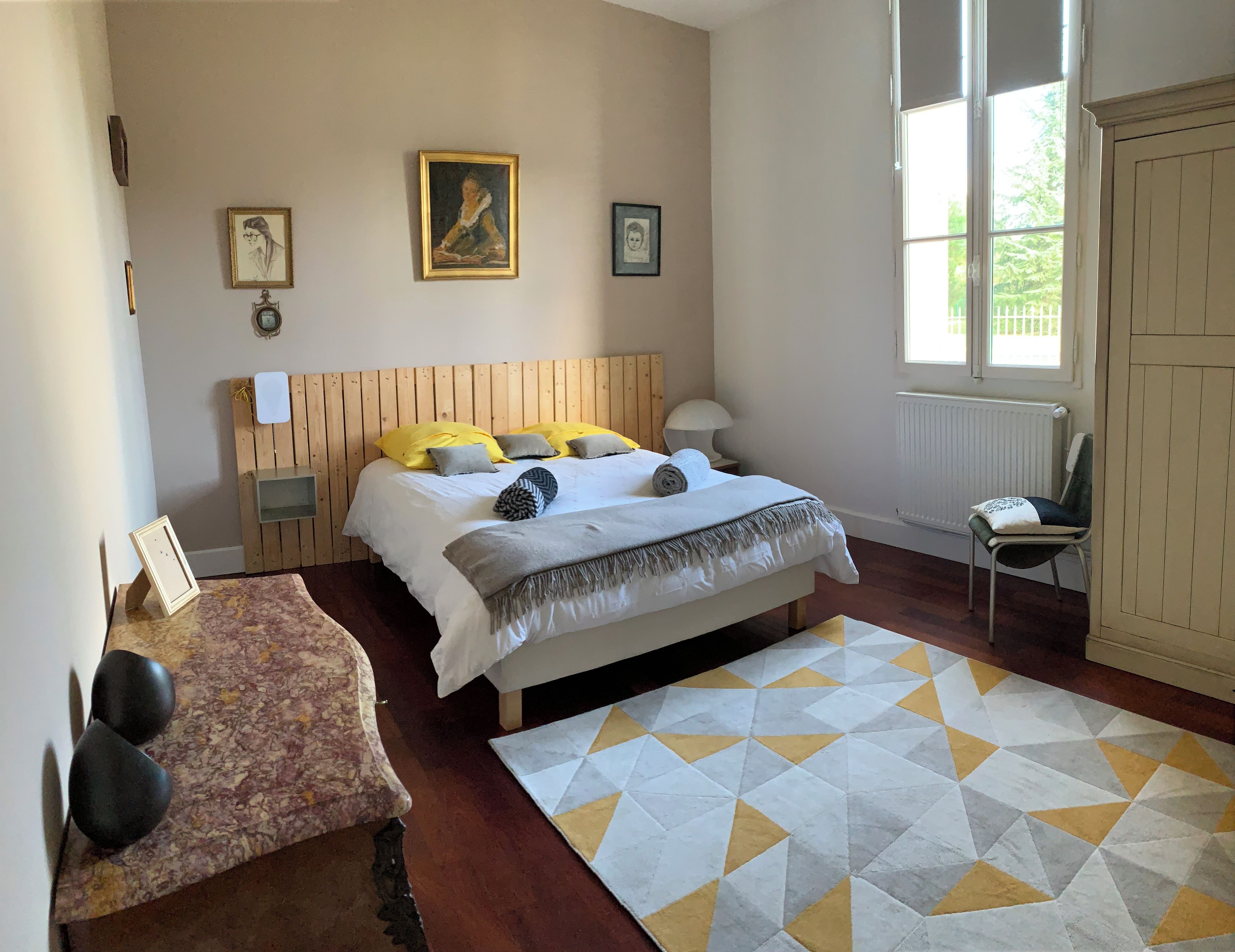 Ein Schlafzimmer mit hölzernem Kopfteil, einem Bett mit mehreren Kissen, einem Nachttisch mit Lampe und einem Teppich mit geometrischem Muster.