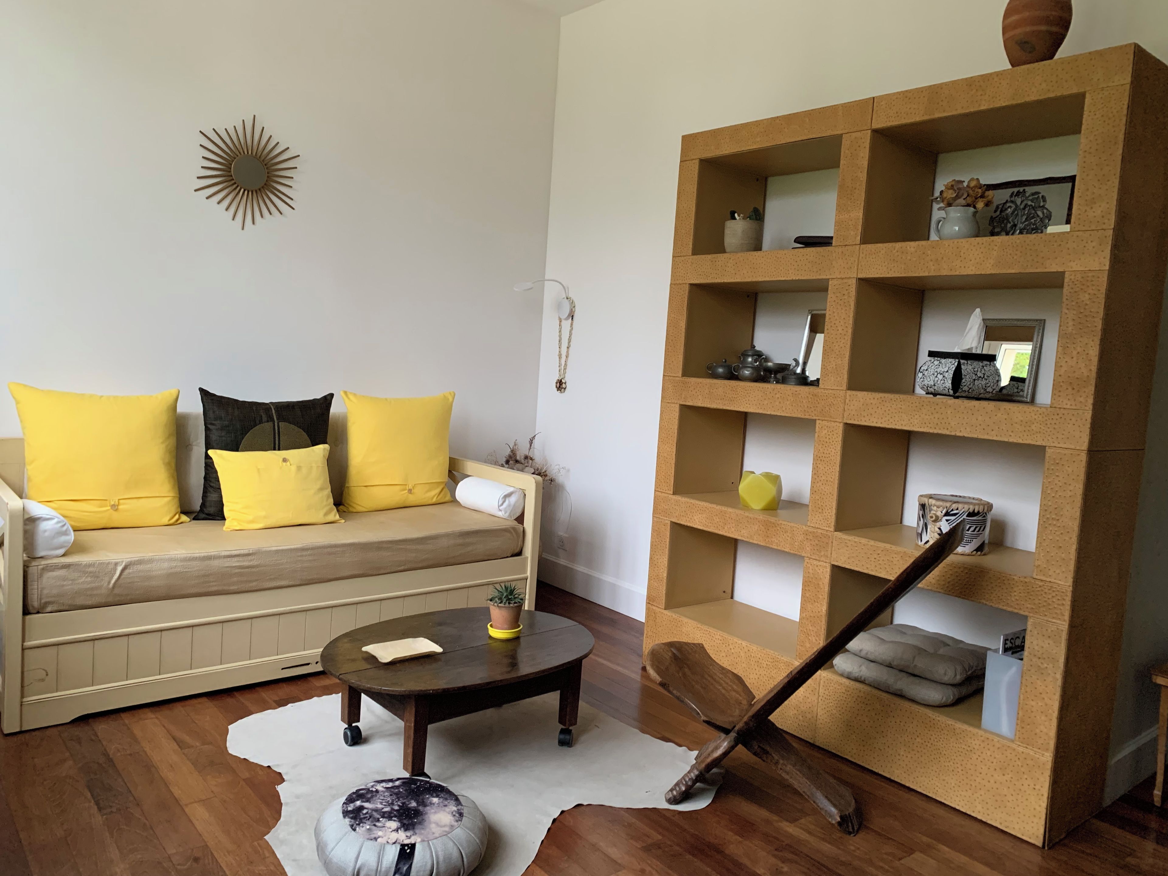 Ein Wohnzimmer mit einer Couch, einem Couchtisch, einem Bücherregal und einem dekorativen Wandkunstwerk im Sonnenstrahl-Design.