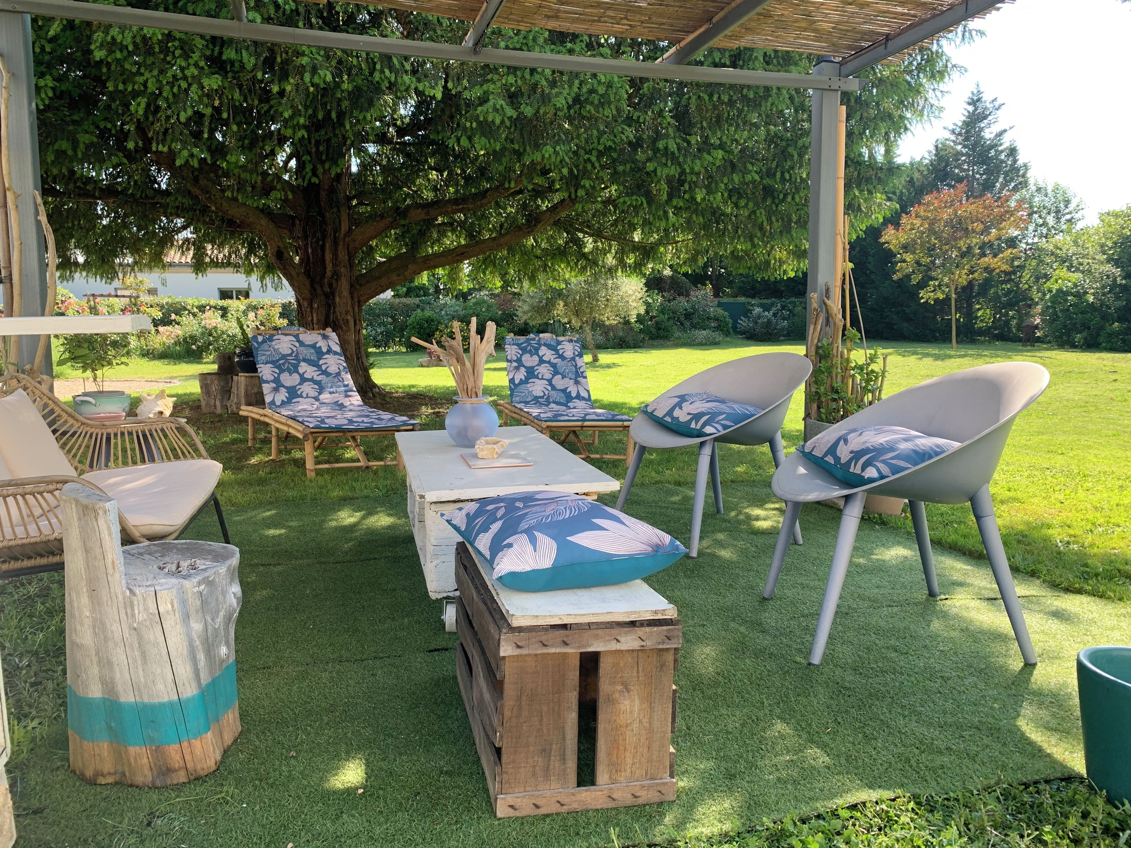 An outdoor seating area with wooden tables and chairs, a large tree, and a grassy lawn.