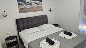 A bedroom with a grey upholstered headboard, white bedding, a painting of waves on the wall, and two black cylindrical objects on the floor. - Seaview 8 Bed Villa Sleeps 16 - Pool & Hot tub (Starigrad)