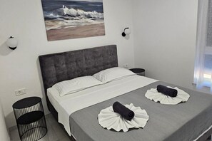 A bedroom with a grey upholstered headboard, white bedding, a painting of waves on the wall, and two black cylindrical objects on the floor. - Seaview 8 Bed Villa Sleeps 16 - Pool & Hot tub (Starigrad)
