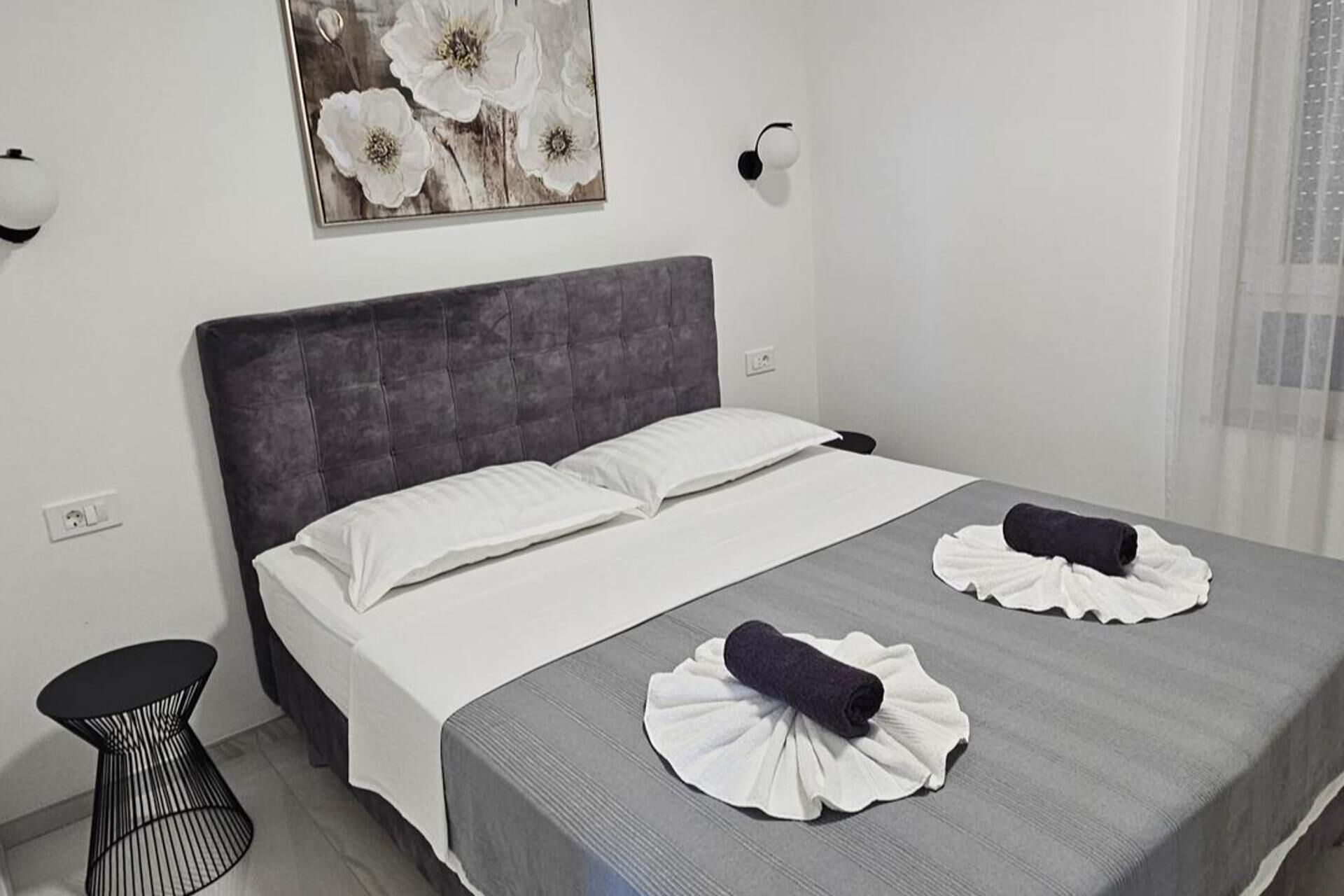 A neatly made bed with white linens, a grey headboard, and two towels on the bed.