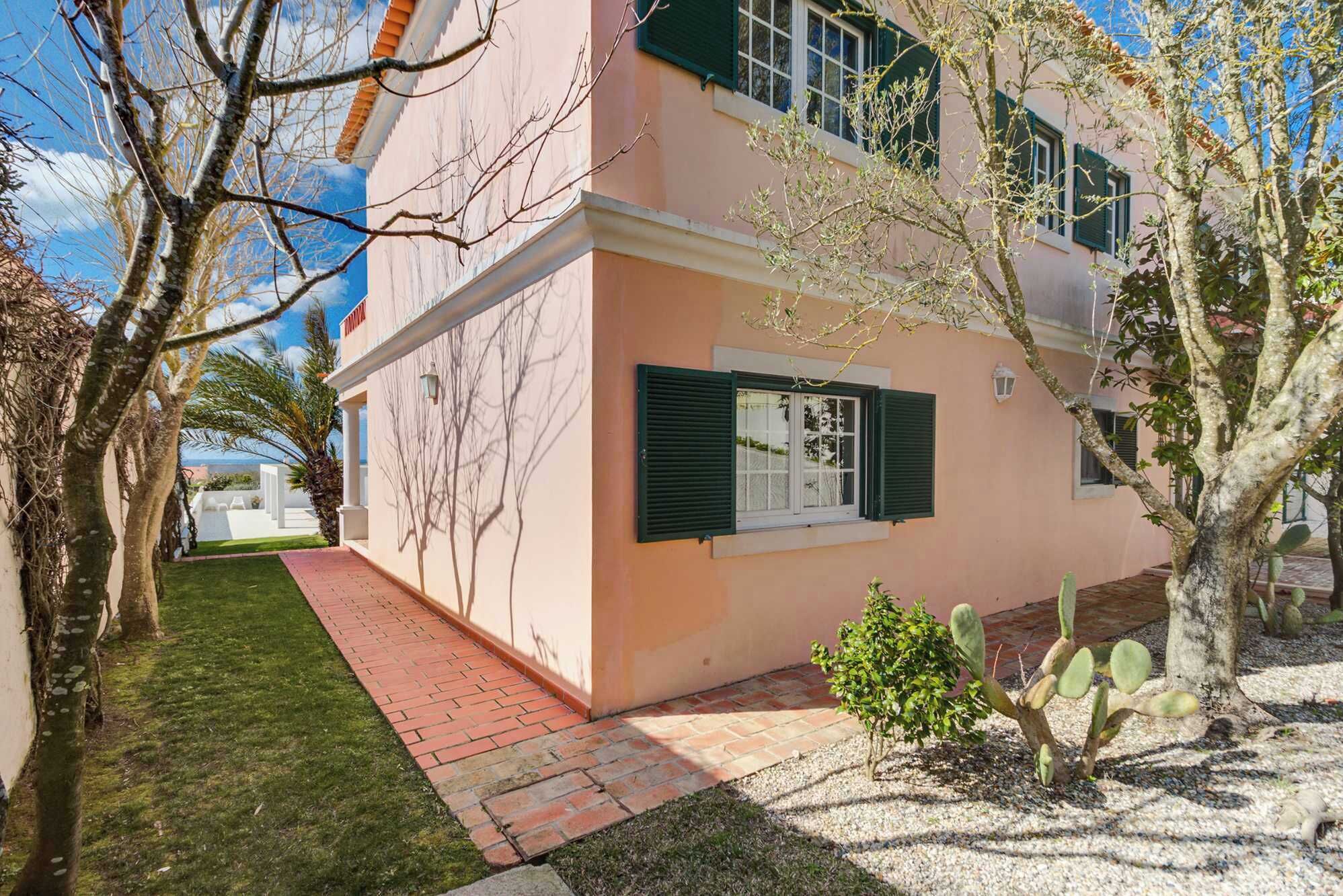 Un edificio de dos pisos con fachada rosa, contraventanas verdes y un camino empedrado que lleva a la entrada.