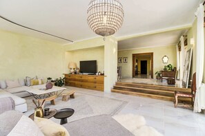 A spacious living room with a large TV, wooden furniture, and a chandelier. - Luxury Coastal Villa with Heated Pool,  Basketball Court & Ocean Views near Lisbon (Atalaia de Cima)