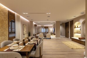 A spacious dining area with a long table set for a meal, a sofa, and a small table with a lamp. - Atrah Elite 3BR Sanctuary in Shuran (Madinah)