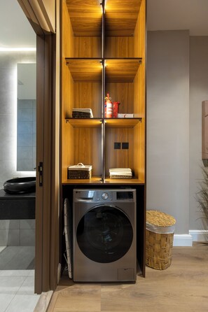A laundry room with a washing machine, a basket, and shelves with items. - Atrah Elite 3BR Sanctuary in Shuran (Madinah)
