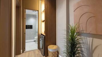 A hallway with a wooden door leading to a bathroom, a woven stool, and a potted plant.