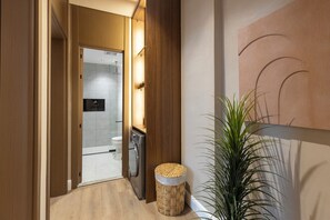 A hallway with a wooden door leading to a bathroom, a woven stool, and a potted plant. - Atrah Elite 3BR Sanctuary in Shuran (Madinah)