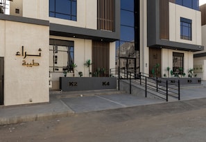 Um edifício moderno com escadaria, vagas de estacionamento numeradas e plantas em vasos.