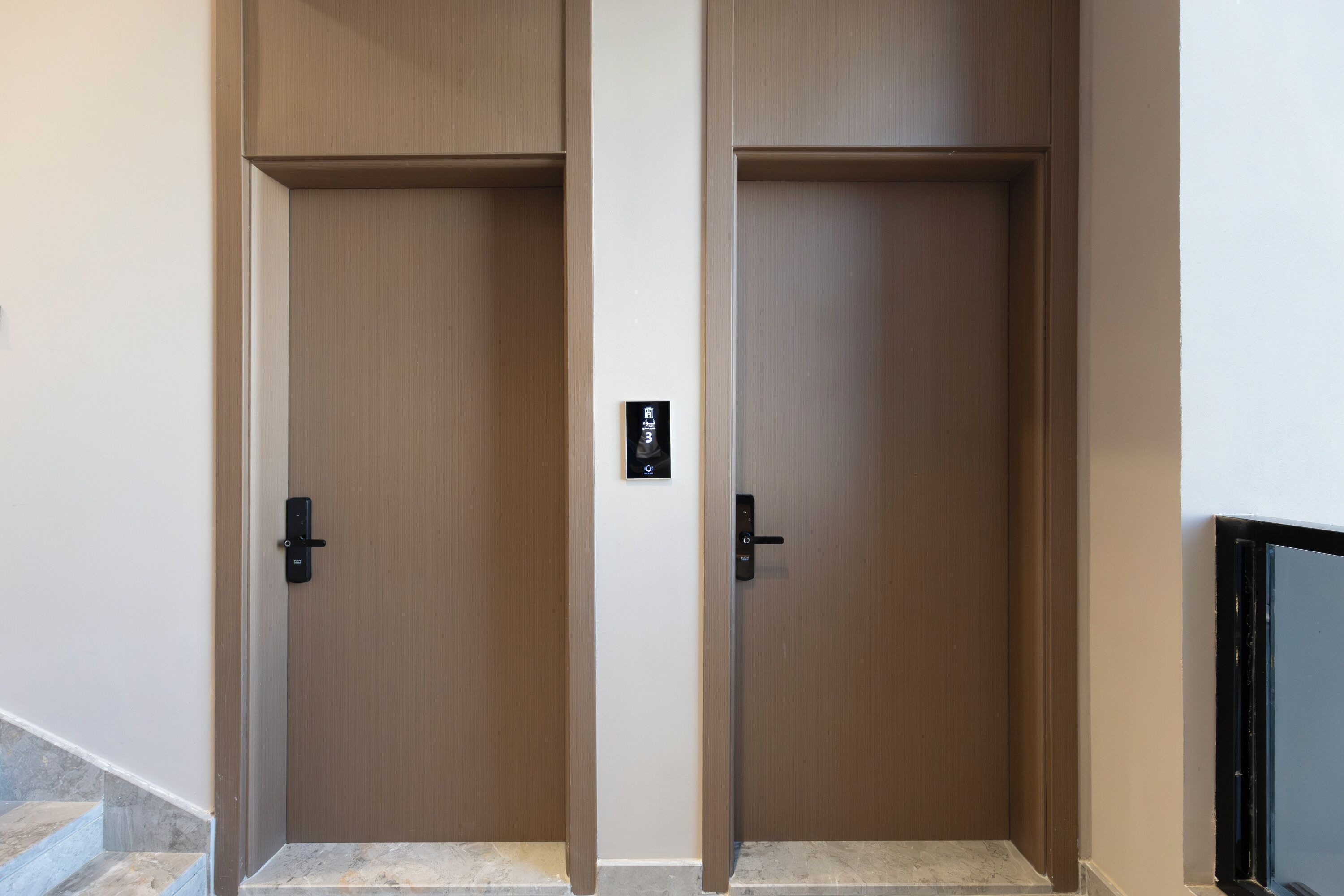 Dos puertas de madera cerradas con un pequeño dispositivo negro en la pared entre ellas.