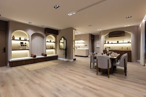 Um interior moderno com área de refeições, prateleiras embutidas com objetos decorativos e iluminação embutida.